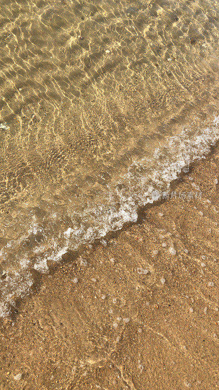 夏日的海滩，清澈平静的海浪拍打着海岸和金色的沙滩，蓝绿色的水反射着蓝天和涟漪，海滩度假，海浪泡沫/泡沫从潮汐和潮湿的沙子在阳光明媚的日子